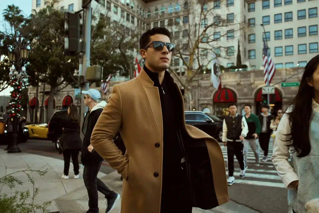 Man in brown coat standing on sidewalk during daytime.