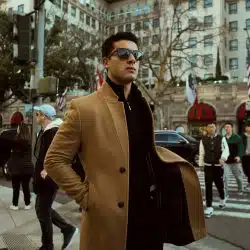 Man in brown coat standing on sidewalk during daytime.