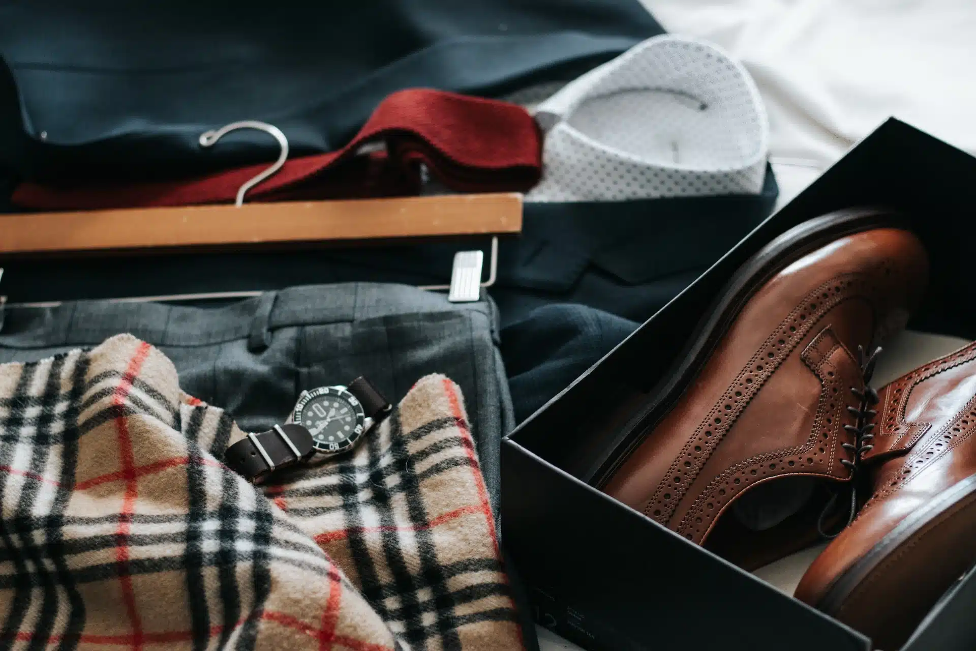 Various men's business attire laying on a bed including a pair of wingtip style footwear.