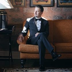 Man in a tuxedo sitting on a brown sofa.