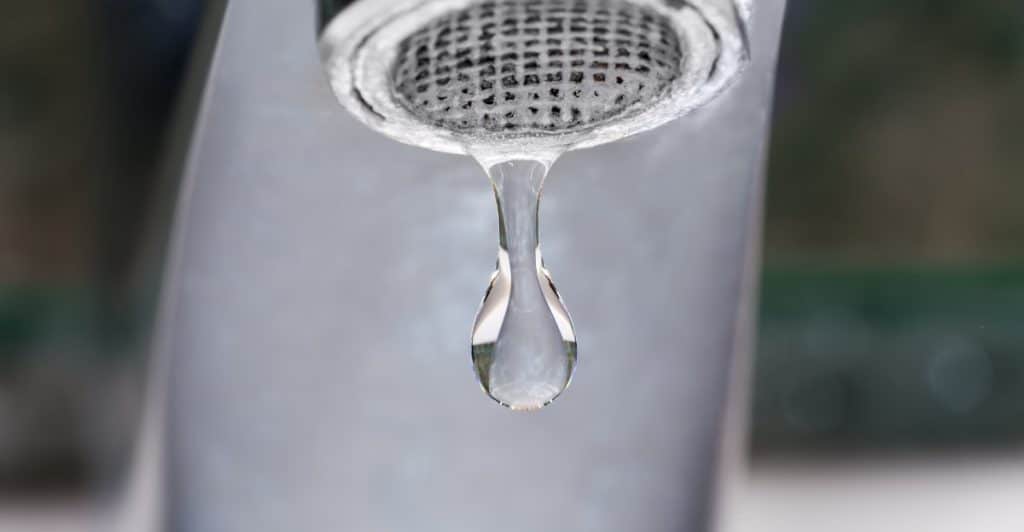 Close-up of a dripping faucet with a large drop of water about to fall.