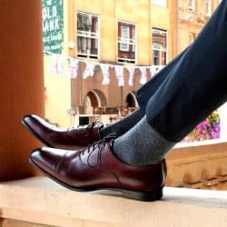 A person's legs and feet resting on a window sill while wearing an oxblood cap toe oxfords