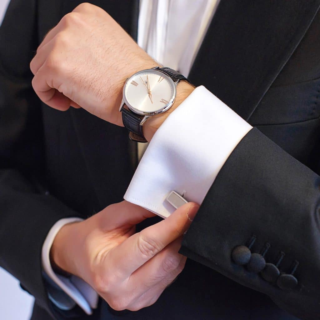 Close up of man adjusting cufflink on white dress shirt under black suit.