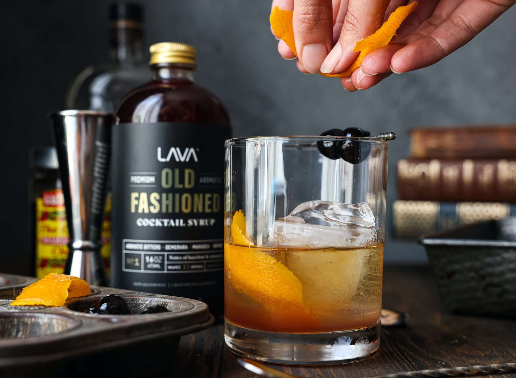 Close-up of a person squeezing an orange peel into an Old Fashioned.