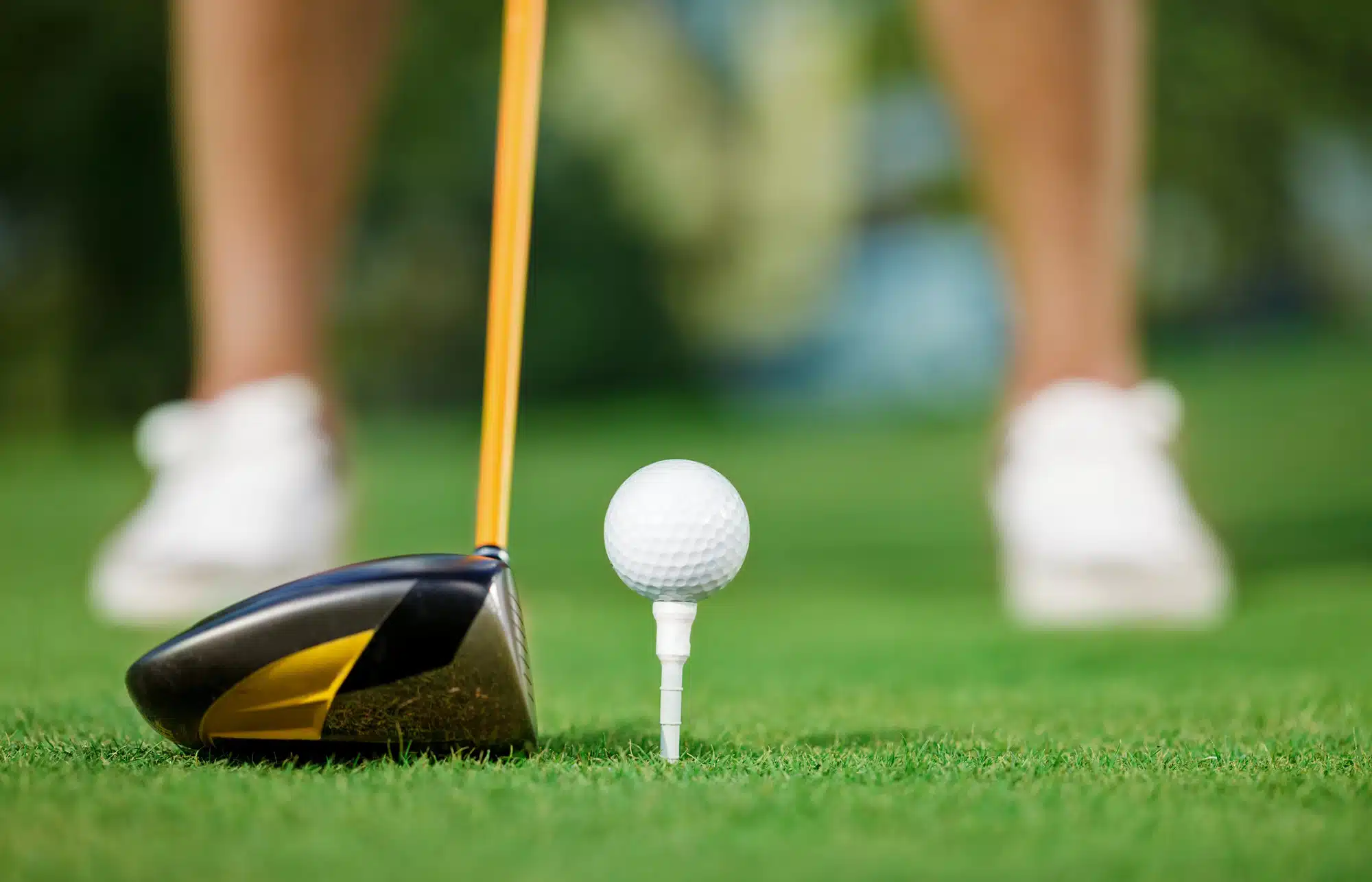 Close-up of a driver golf club next to a golf ball on a tee on a green