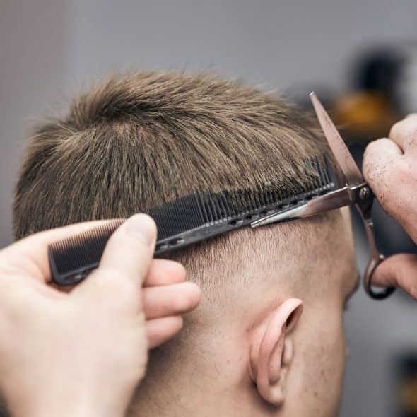 A close-up of a person's head while a barber uses a comb and scissors to cut their hair.