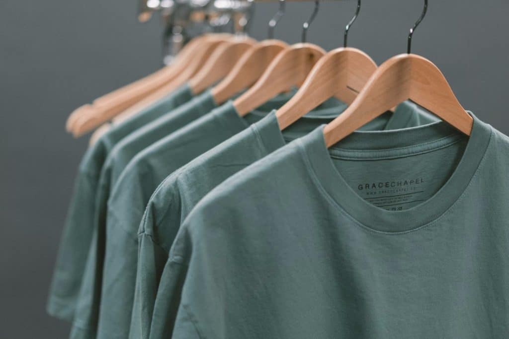 Row of Green t-shirts on wooden hangers.