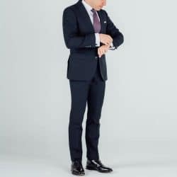 A man wearing a black suit with black oxford dress shoes looking at his wristwatch.