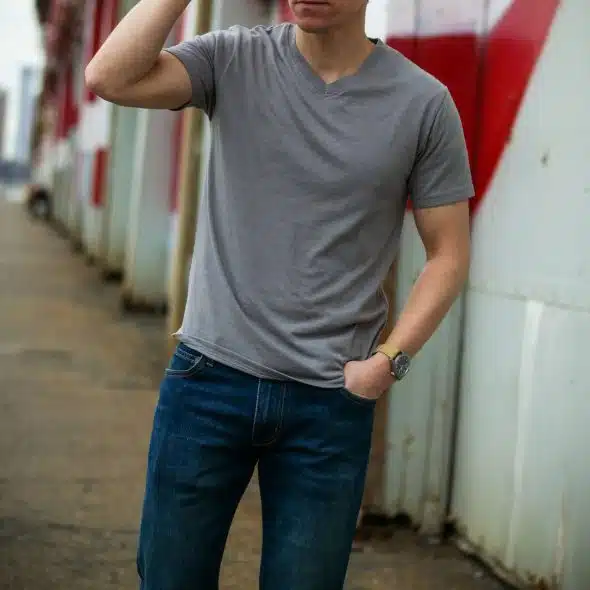 A man wearing a gray v-neck t-shirt and blue jeans, with a watch on his left wrist.