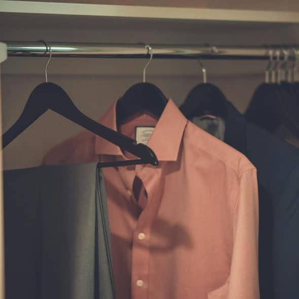 A close-up of pink and black dress shirts with gray pants hanging on black hangers in a closet