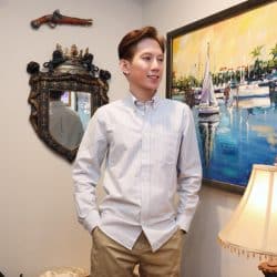 A man standing in a room with a painting and a mirror, wearing a light-colored striped shirt and tan pants.