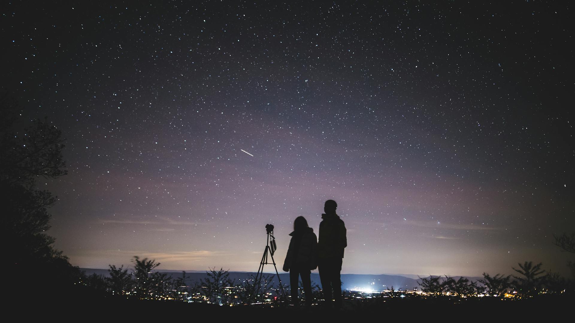 A couple stargazing standing under a starry sky.