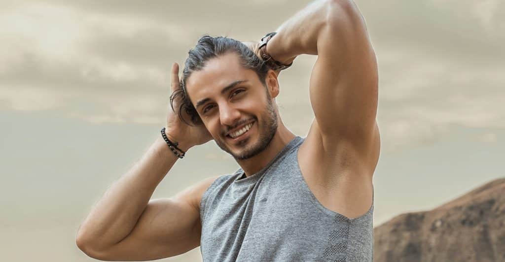 A smiling muscular man with hands behind his head.