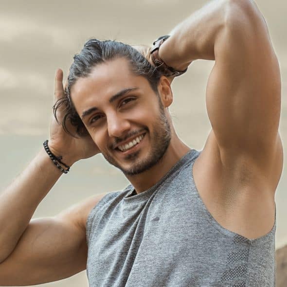 A smiling muscular man with hands behind his head.