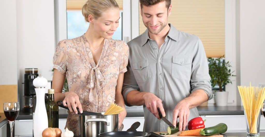 Couple preparing food in a kitchen, with the man cutting vegetables.