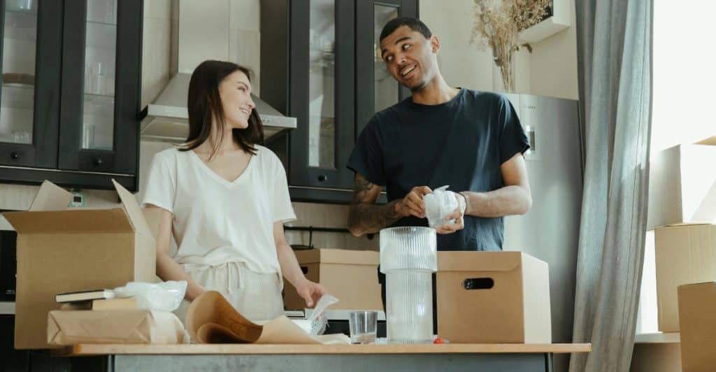 Man and woman talking while packing household items, with cardboard boxes scattered around them.