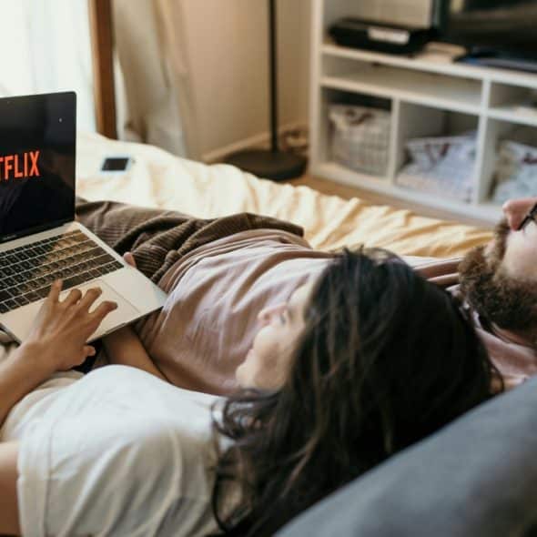 A couple relaxing in bed, watching Netflix on a laptop.