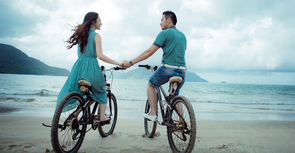 Couple cycling by the sea while holding hands.