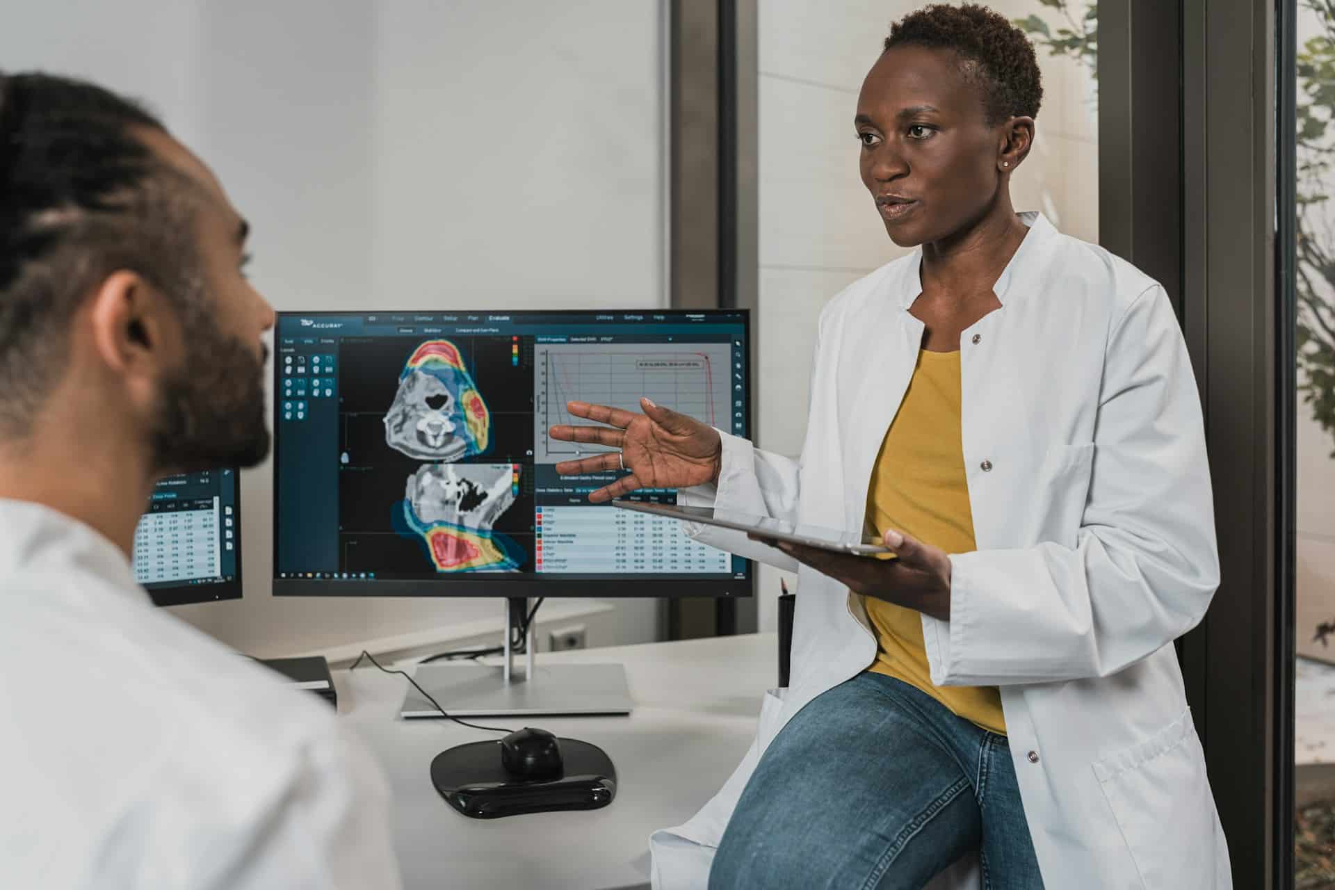 A doctor and a patient are engaged in conversation while a nearby monitor displays medical imagery.