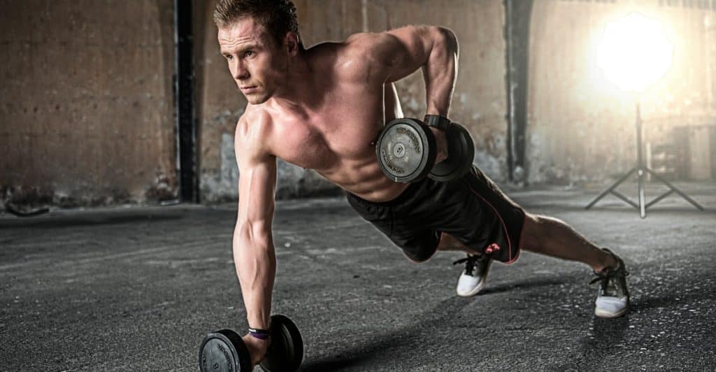 Shirtless muscular man working out with dumbbells on asphalt.