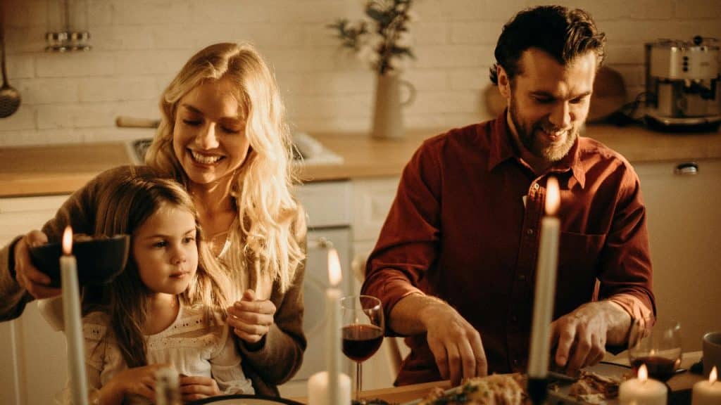 A happy family of three having dinner, with lit candles placed on the dinner table.