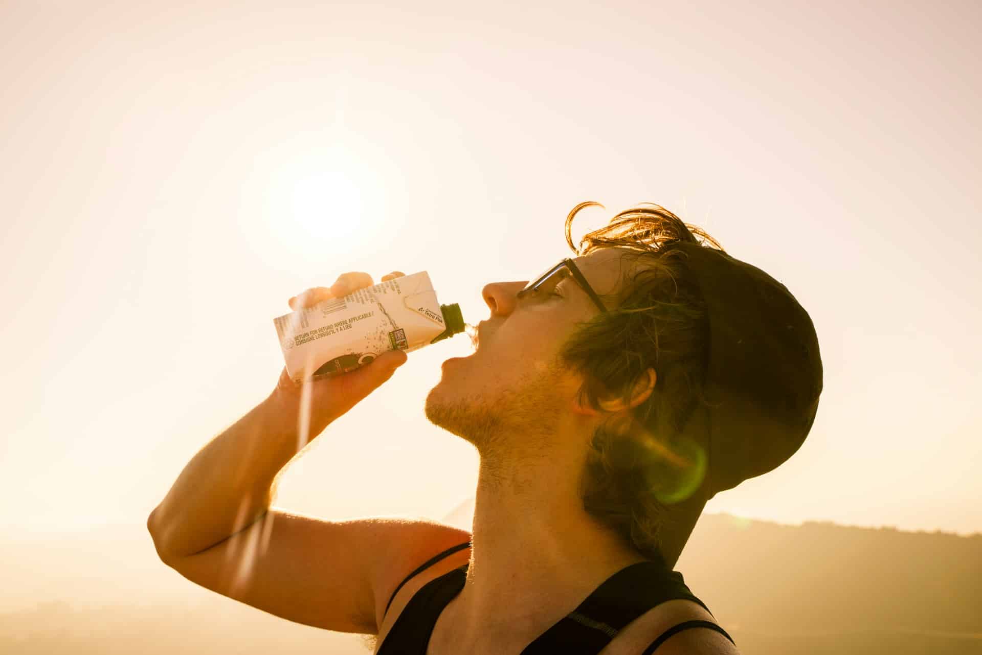 A man wearing spectacles drinking water from a bottle with his eyes closed.