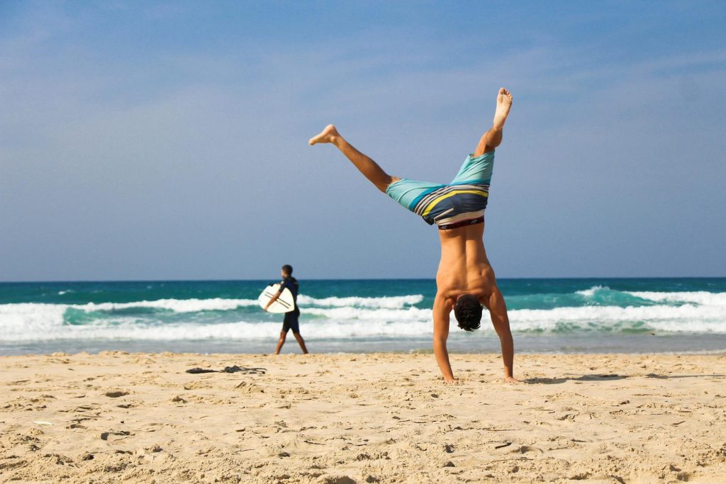 Shirtless man cartwheeling at the beach.