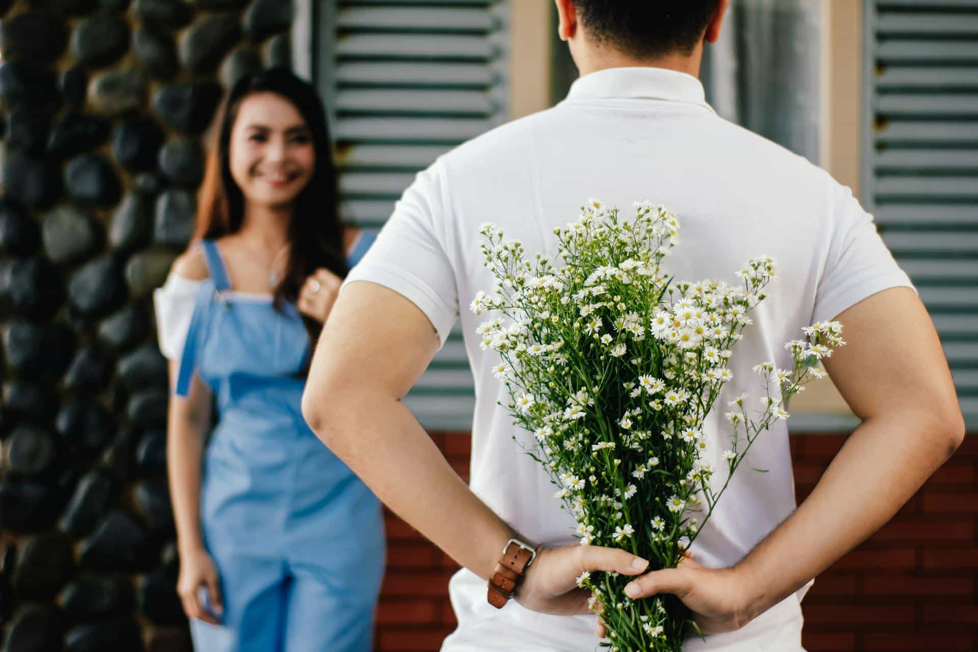 A man hiding flowers behind his back from his partner.