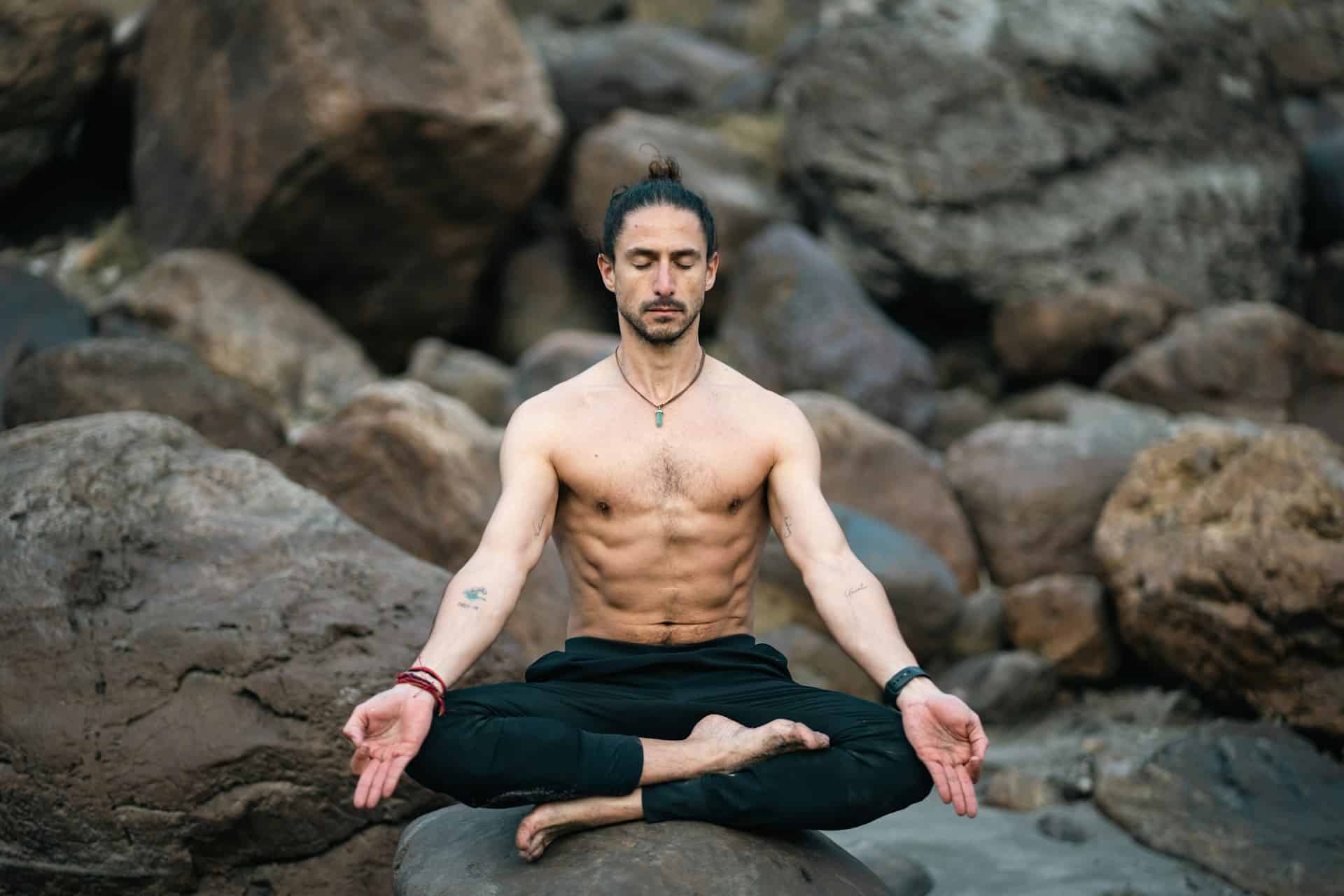 A shirtless man meditating on a rock.