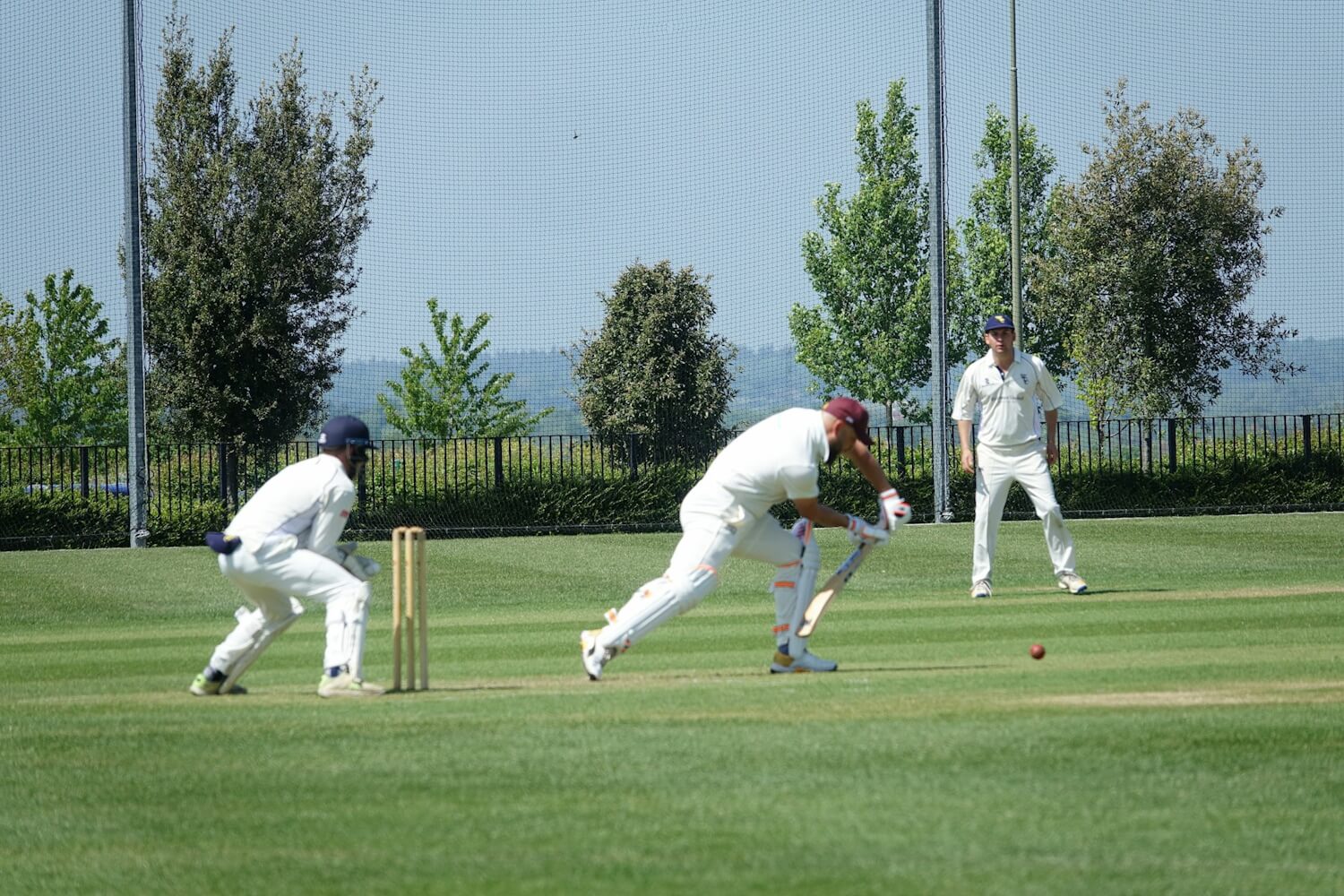 People playing cricket with the batsman defending the ball.