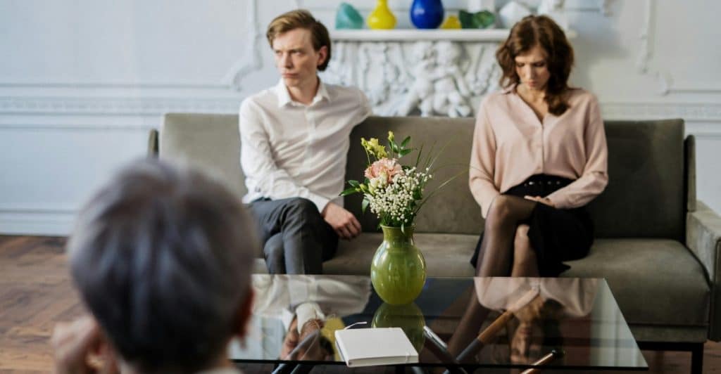 A couple is sitting on a couch in a therapist's office, looking away from each other