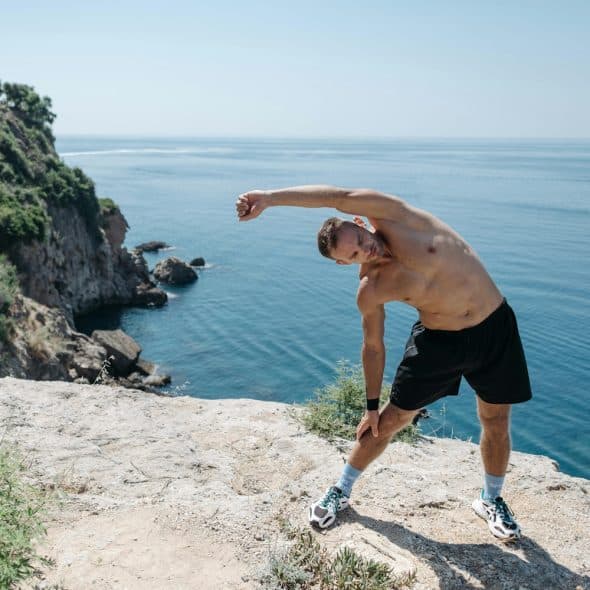 A man stretching on a cliff overlooking the ocean.