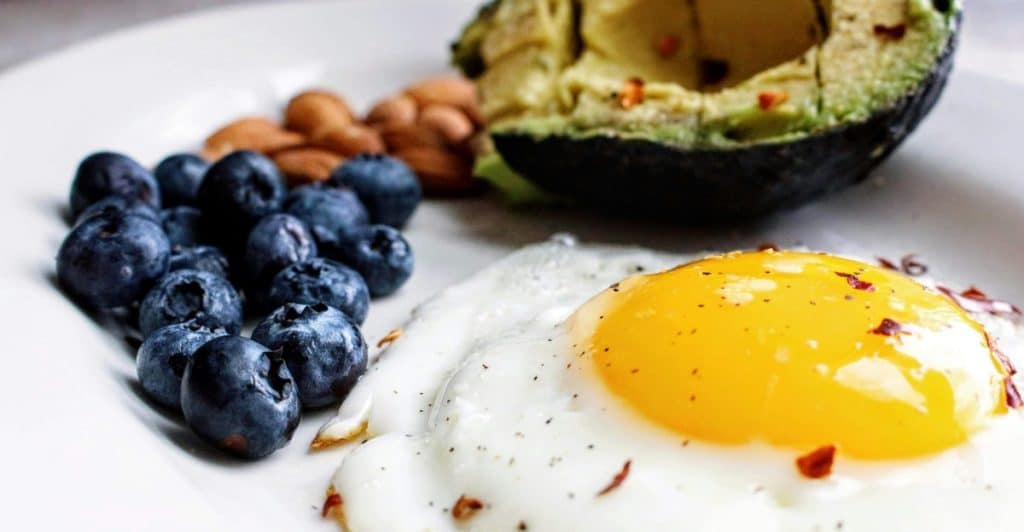A close-up of a breakfast plate with a fried egg, blueberries, almonds, and half an avocado.