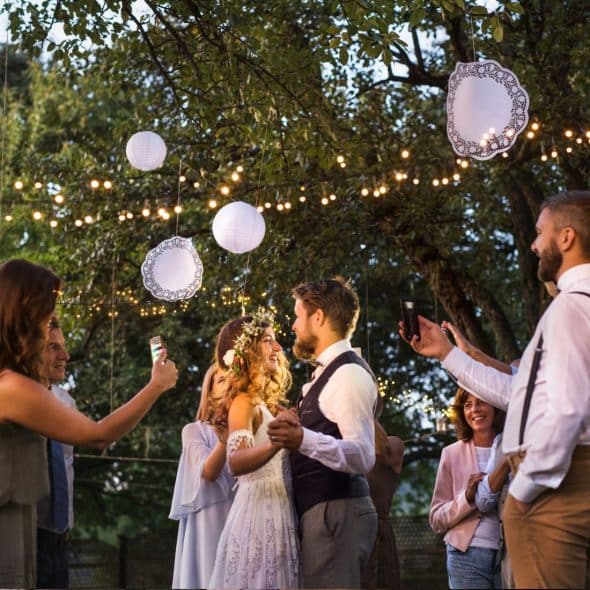 A bride and groom sharing a dance at their outdoor wedding reception as guests capture the moment with their smartphones.