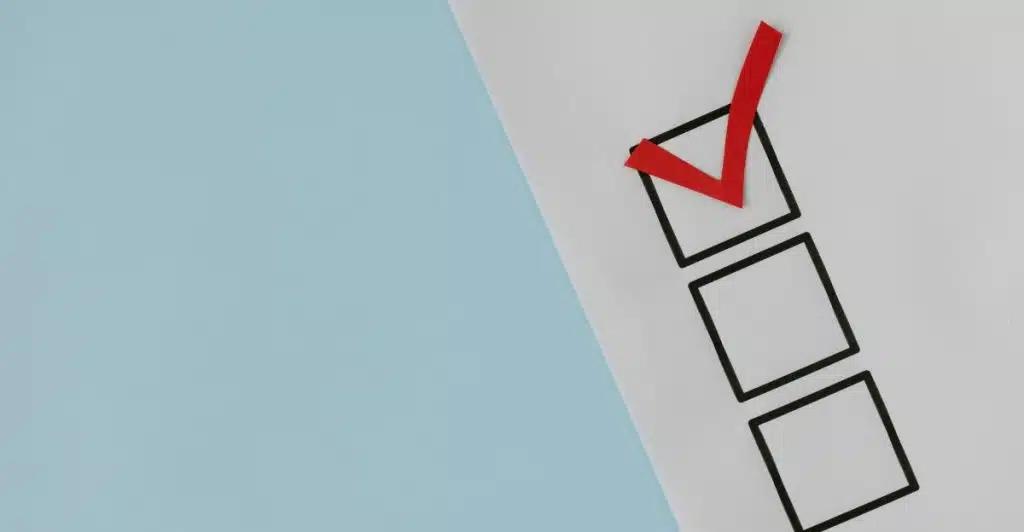 A piece of paper with three empty square checkboxes and a red checkmark in the first box is on a light blue background.