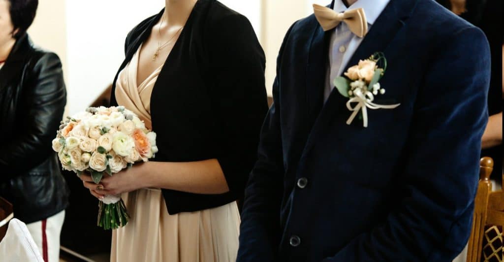 A close-up shot of a couple standing during a wedding ceremony, showcasing their elegant and complementary outfits.