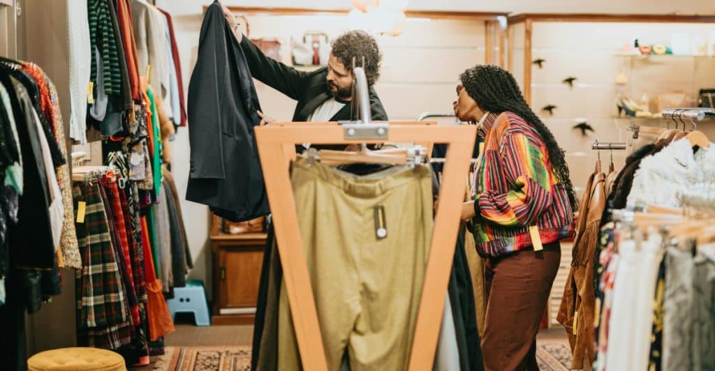  A couple shopping together in a vintage store, looking through racks of clothing.