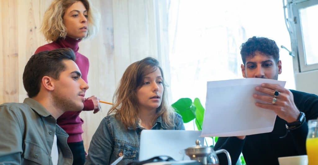 Four people gathered around a table, looking at documents and working together.