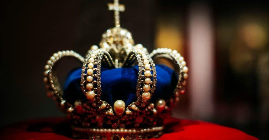 A close-up of a blue jeweled crown placed on a red cushion.
