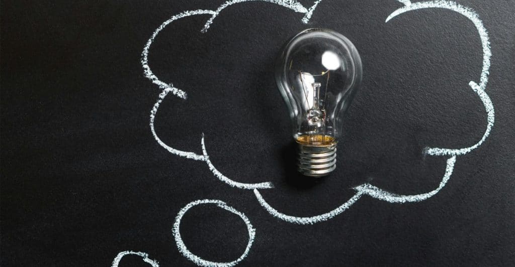 A lightbulb is inside a chalk-drawn thought bubble on a dark background.