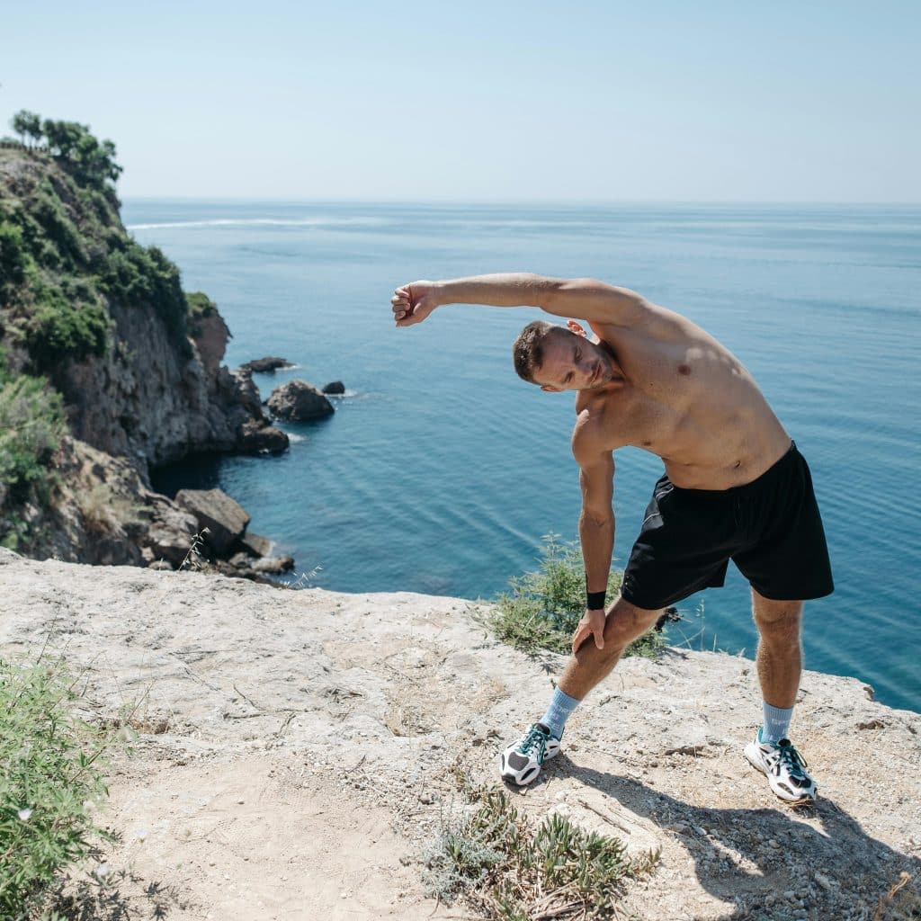 A man stretching on a cliff with the ocean in the background.