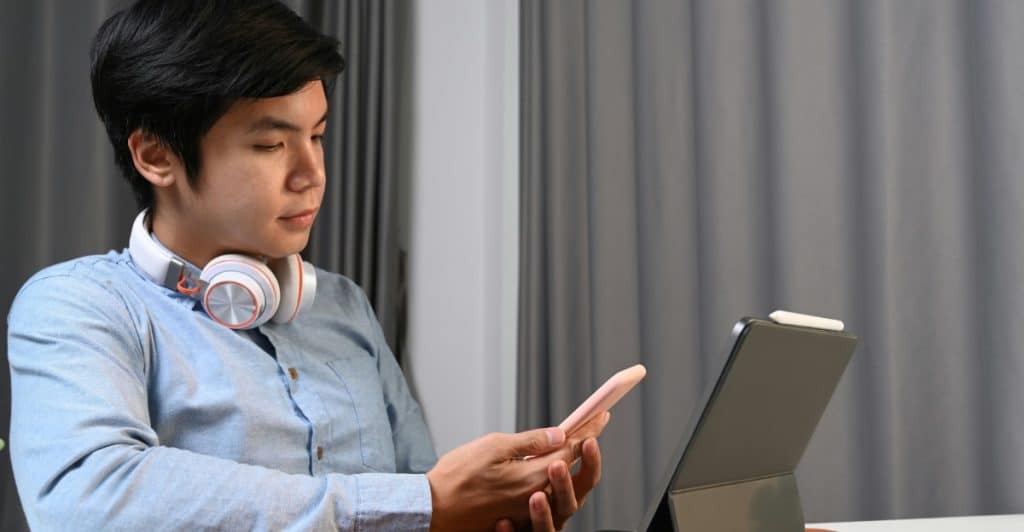 A person wearing headphones around his neck, looking at a smartphone and a tablet.