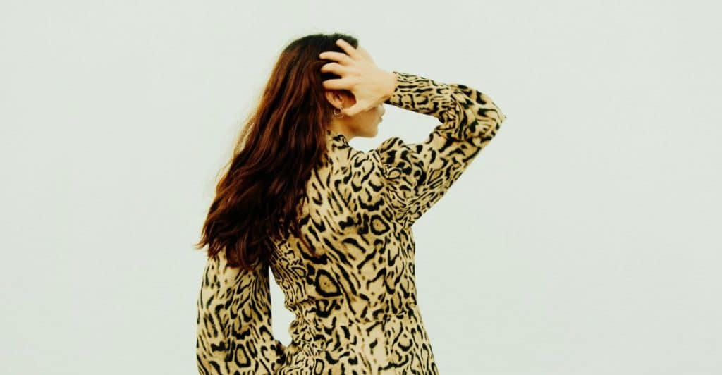 A person with long brown hair, wearing a leopard print dress, partially turned away from the camera.