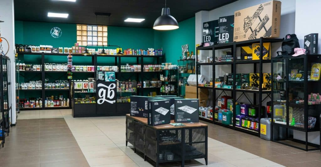 The interior of a store with shelves stocked with various products, black metal display tables, and a teal accent wall.