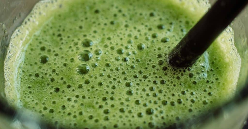 Close-up of bubbly green aloe vera juice with a straw in a glass.