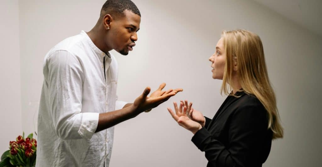 A man and a woman are standing and arguing, gesturing with their hands.