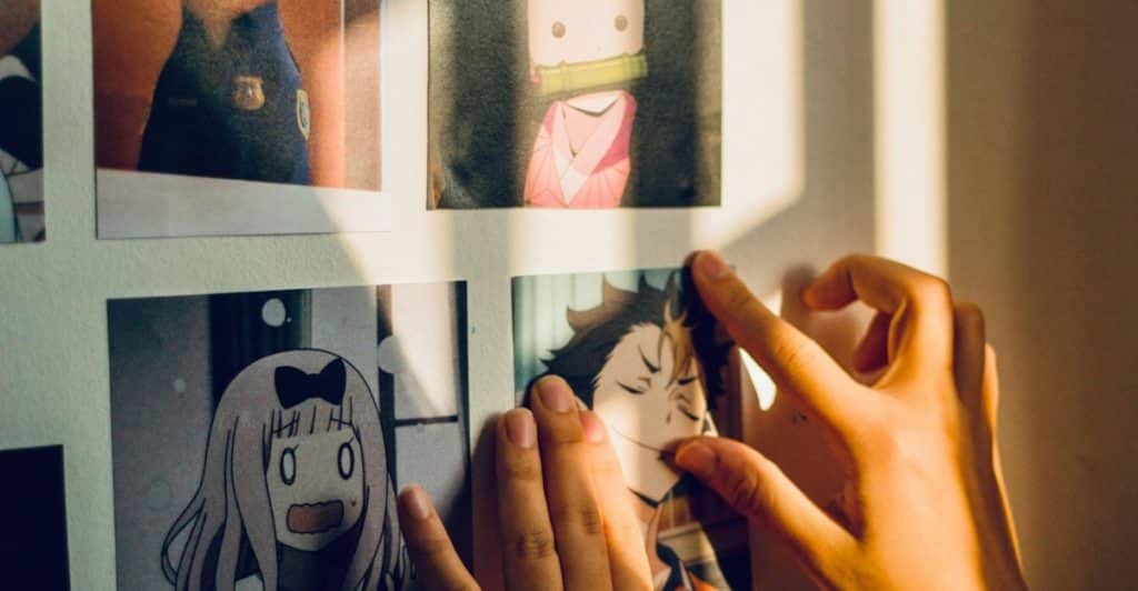 Hands placing anime-themed photos on a wall.