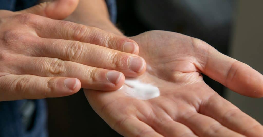 A person is rubbing a small amount of white cream into the palm of their hands.