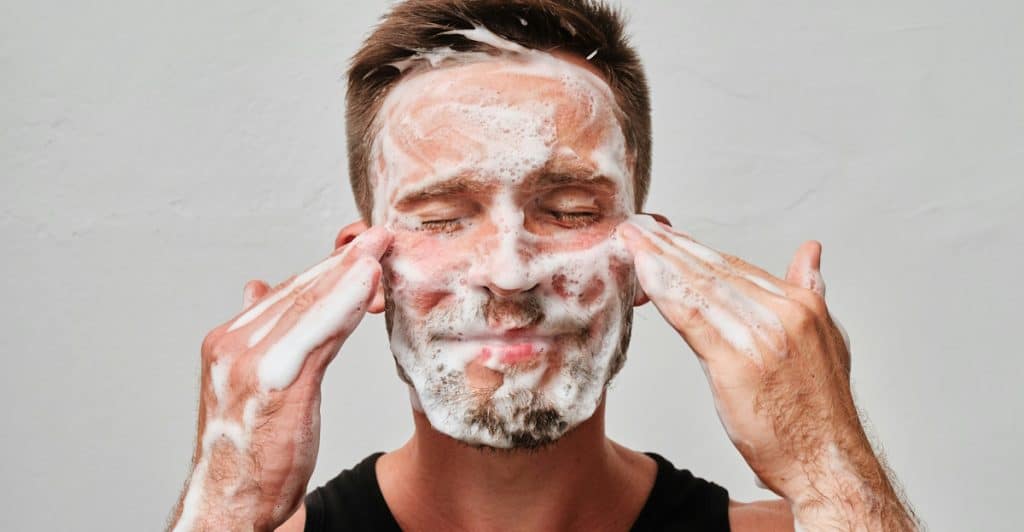 A person applying facial cleanser with foam to their face.