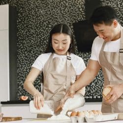 Asian couple in matching shirts and aprons baking together in a kitchen..